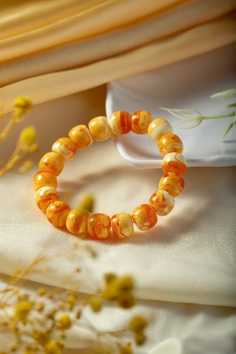 Decorative bracelet with orange and yellow beads on a textured surface with flowers.
