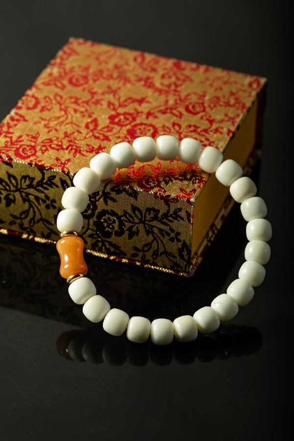 White beaded bracelet with an orange bead on a decorative box