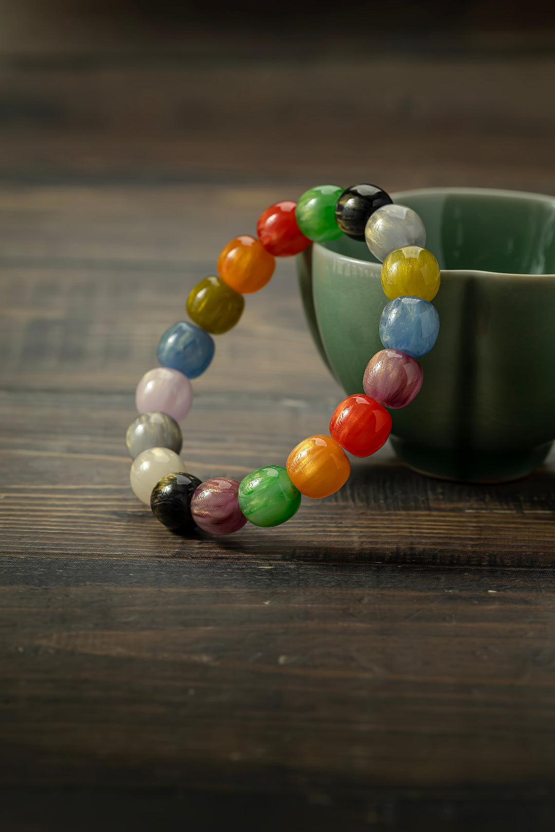 Colorful beaded bracelet on a wooden surface with a green cup in the background