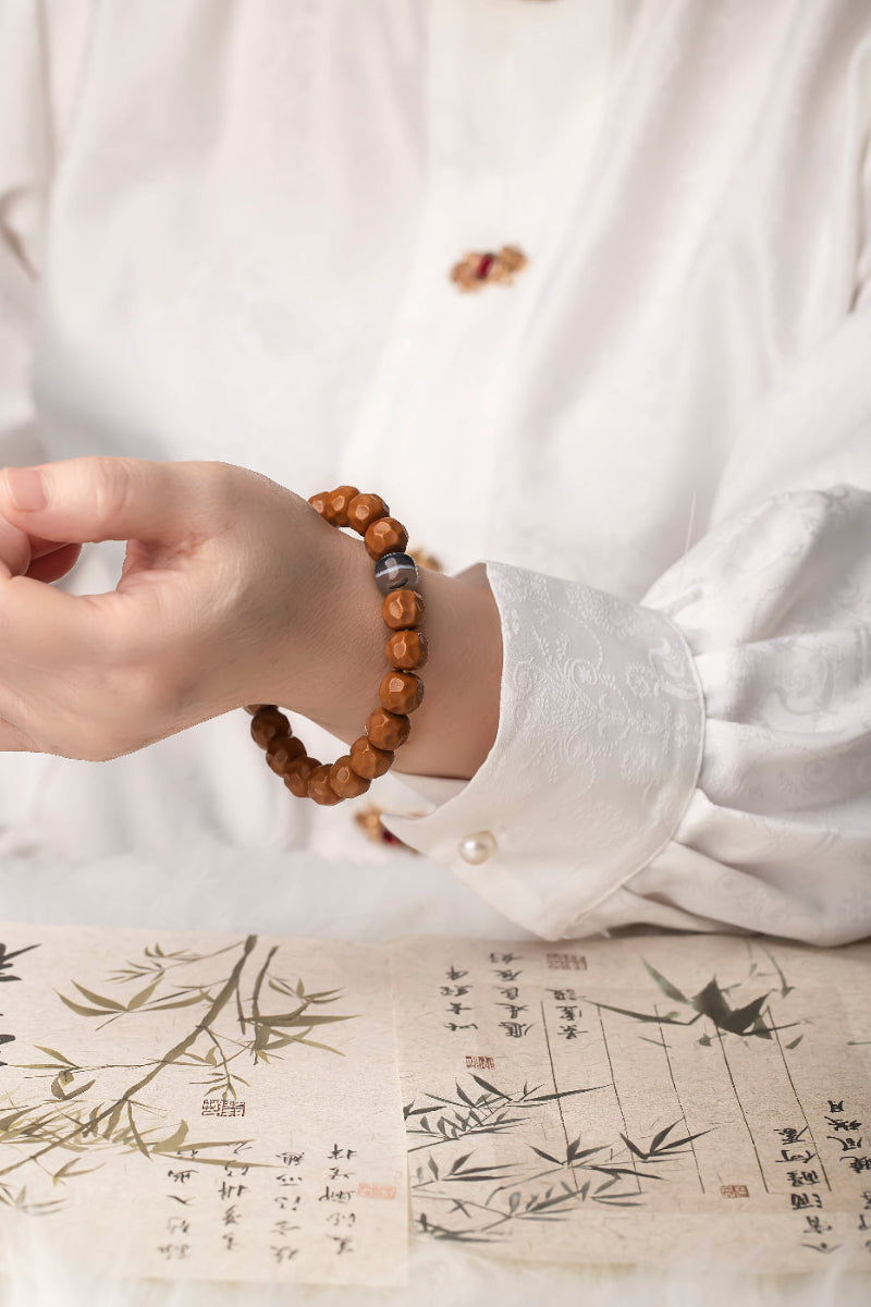 Hand wearing a wooden bead bracelet on a white shirt with a traditional design background