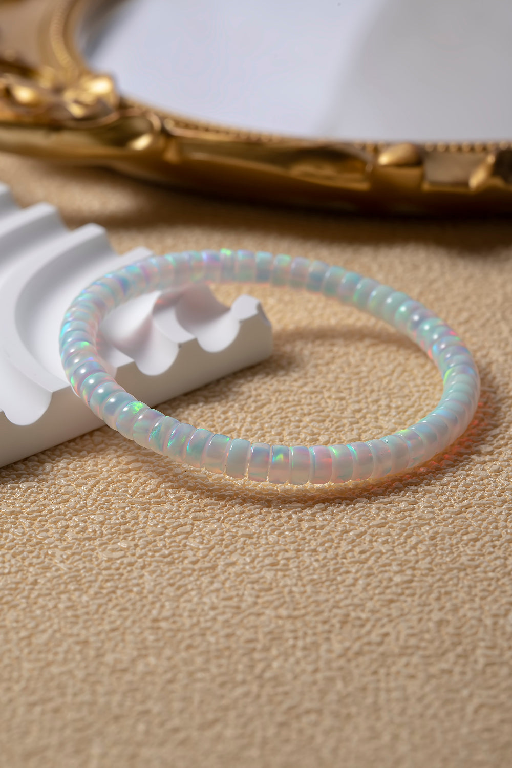Opal beaded bracelet on a beige surface with a gold ring and white object in the background